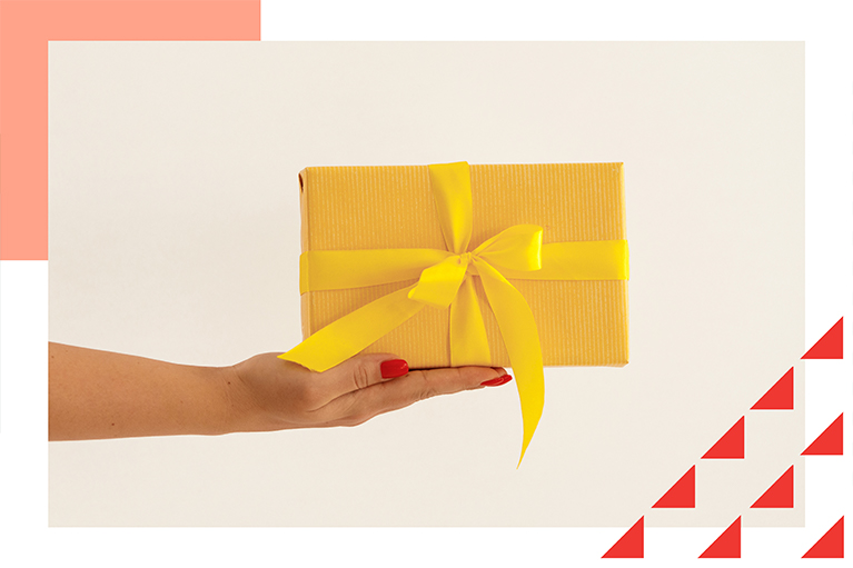 female hand holding small yellow gift box with a bow